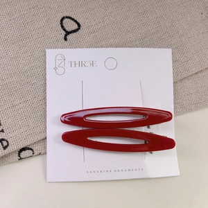 Detail view of two dark red oval hollow hair clips on a white display card stand