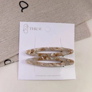 Detail view of acetate hollow oval hair clips with cream marble pattern on display card