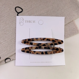 Detail view of two hollow oval leopard print acetate hair clips on display card