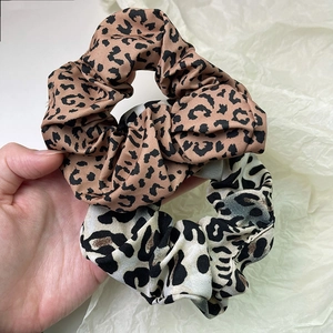 Detailed view of two leopard print scrunchies in brown and cream held in hand
