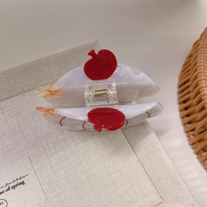 Detail of acetate hair claw with red apple and star charms on beige linen background