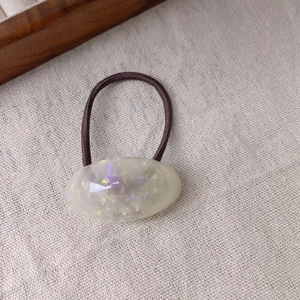 Detail of oval cream resin hair tie with shimmering sequins and Sanshine logo