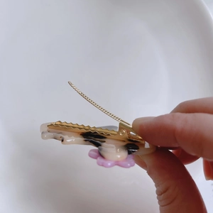 Dettaglio del fermaglio per capelli gatto marmorizzato con fiore rosa e molla aperta