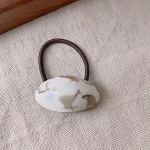 Detailed macro shot of oval marble pattern acetate hair tie with Sanshine brand logo