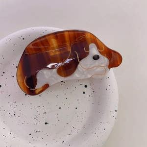 Détail d'une pince à cheveux en acétate brillant au motif de chien cartoon marron et blanc