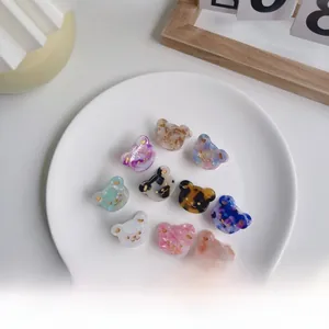 Détail de dix mini pinces à cheveux ours en acétate avec feuilles d'or sur un plat blanc