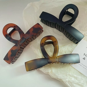 Three elegant large bow-shaped hair claws in black, tortoiseshell, and amber on white paper