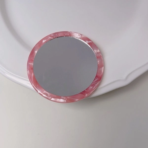 Close-up of portable pink marble pattern acetate vanity mirror on a white tray