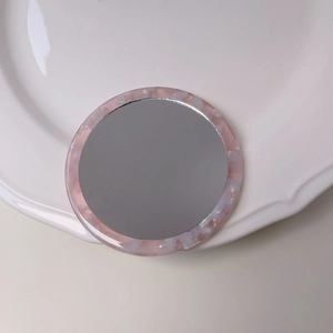 Detailed macro view of portable pink marble acetate round compact mirror on a ceramic plate