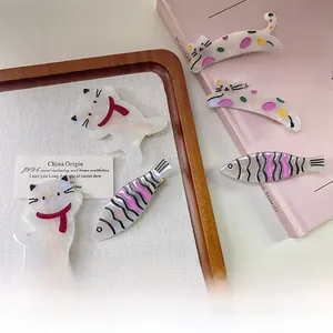 Détail de cinq jolies barrettes en acétate avec motifs chat et poisson sur un livre