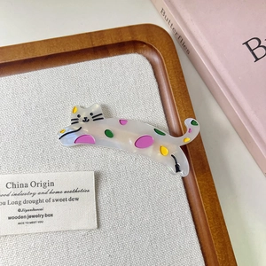 Détail d'une pince à cheveux chat en acétate blanc avec des pois colorés sur plateau en bois