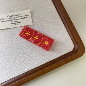 Détail d'une pince à cheveux rouge marbrée avec des motifs dorés pour le nouvel an