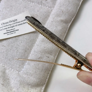 Detailed close-up of a vintage grey marble resin hair clip with a golden metal base