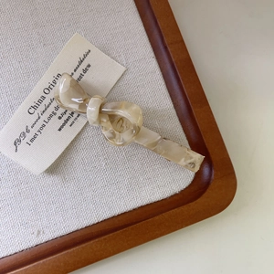 Dettaglio di un fermaglio per capelli a fiocco in acetato marmorizzato crema su vassoio