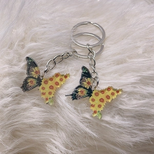 Detailed view of two artistic butterfly keychains on soft white faux fur background