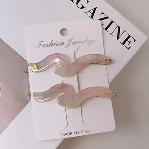 Close-up of wavy acetate hair clips in iridescent pink and cream on a fashion magazine
