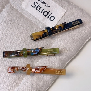 Three acetate bow hair clips in tortoiseshell and marble patterns with gold lettering