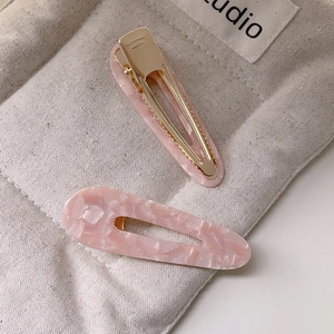 Détail de barrettes à cheveux en acétate rose marbré avec base en métal doré sur toile