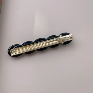 Detailed view of black resin spherical charms on a golden metal hair clip base