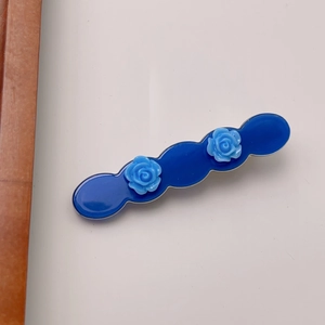 Detail of navy blue wavy hair clip featuring light blue relief rose flowers and glossy finish