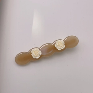 Close-up of wavy acetate hair clip in amber brown with delicate 3D white rose flowers