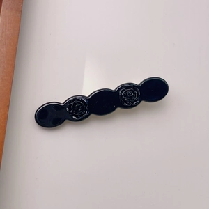 Detailed close-up of a black acetate rose hair clip with elegant relief patterns