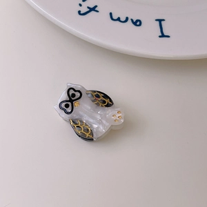 Close-up of owl hair clip with white marble texture and black-gold feather details