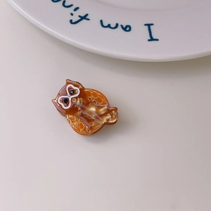 Detailed close-up of an owl-shaped hair claw clip with amber marble texture and gold detailing