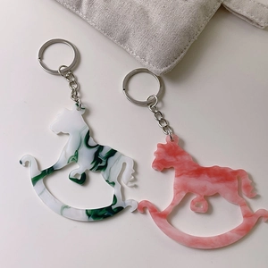 Detail of acrylic rocking horse keychains with marble patterns in green and pink colors