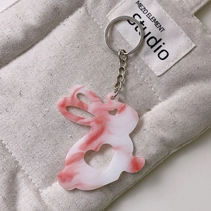 Détail du porte-clés lapin en acrylique marbré rose avec découpe cœur sur sac gris