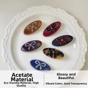 Detailed view of handmade acetate oval hair clips with rhinestone bows in a ceramic plate
