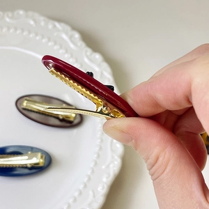 Close-up of elegant oval resin hair clips with rhinestone bow on a white ceramic plate