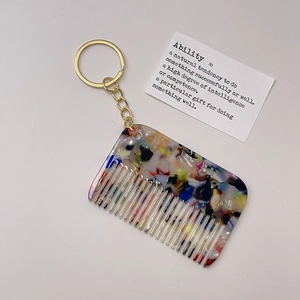 Detail of a floral acetate comb keychain with gold hardware on a minimalist card