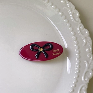Detail of burgundy oval hair clip with black bow and gold France Handmade lettering