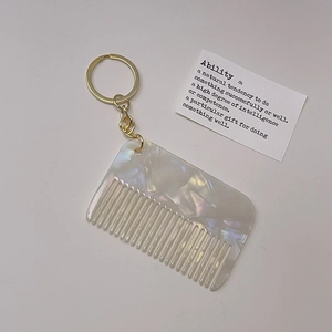 Detail of mini acetate comb keychain with iridescent pearl texture and gold ring