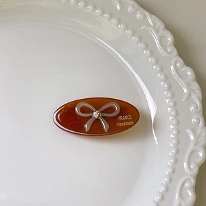 Detail of a brown amber oval hair clip with a rhinestone bow on a white ceramic plate