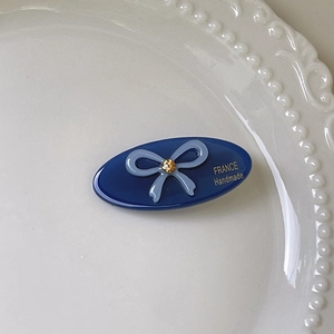 Detail of blue oval hair clip with bow, rhinestone and France Handmade logo on plate