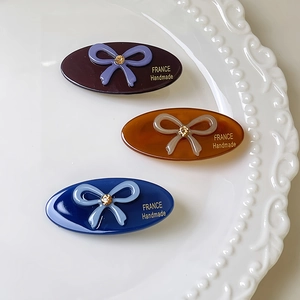 Three elegant oval hair clips with rhinestone bows in purple, amber, and deep blue colors