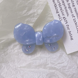 Dettaglio del fermaglio a farfalla in acetato blu con cristalli e logo dorato