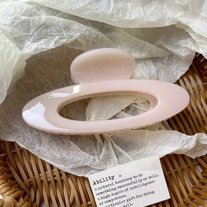 Close-up of a pale pink hollow oval hair claw clip on white textured paper