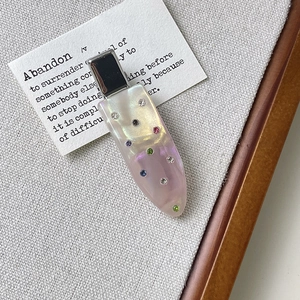 Macro shot of acetic hair clip with multicolored crystals on a grey textured surface