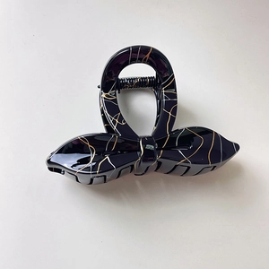 Detail of black bow hair claw clip with golden marble texture and durable metal spring