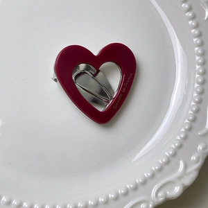 Detail of burgundy heart hair clip with gold text on a white ceramic plate