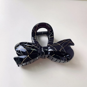 Detailed close-up of glossy black lace-patterned bow hair claw clip with golden veins