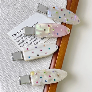 Detail of four acetate hair clips with colorful rhinestones on a textured grey fabric