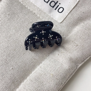 Détail d'une petite pince à cheveux noire avec strass colorés sur fond de toile