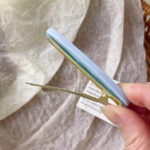 Dettaglio macro di un fermaglio in acetato azzurro con clip in metallo dorato