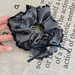Close-up of grey scrunchie with black lace trim and embroidered bows for hair