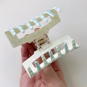 Detail of a large cream hair claw clip with light blue plaid pattern held in hand