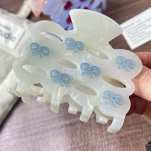 Elegant white acetate hair claw with blue bow pattern and wavy hollow design